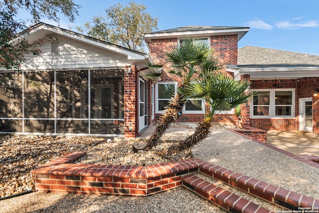 rear view of property with brick siding, a shingled roof, and a sunroom