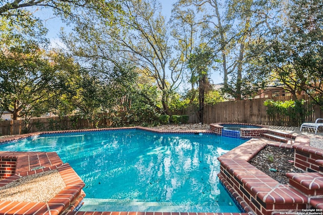 view of swimming pool with a fenced backyard and a pool with connected hot tub