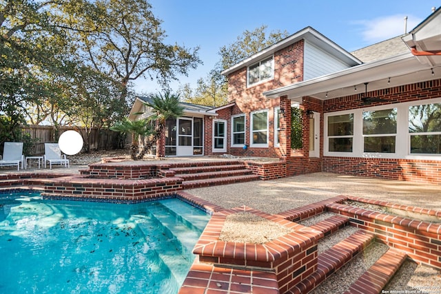 exterior space with a fenced in pool, fence, a sunroom, a patio area, and brick siding