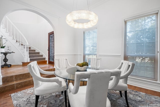 dining area with arched walkways, crown molding, stairs, and wood finished floors