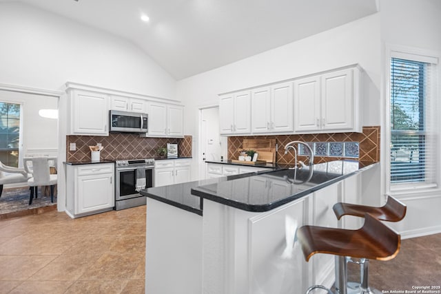 kitchen with a breakfast bar, a peninsula, a sink, stainless steel appliances, and white cabinetry