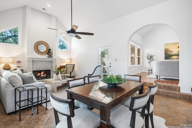 dining area featuring visible vents, high vaulted ceiling, a glass covered fireplace, arched walkways, and ceiling fan