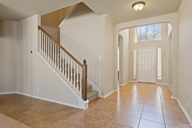 foyer with baseboards, stairs, arched walkways, a towering ceiling, and tile patterned floors