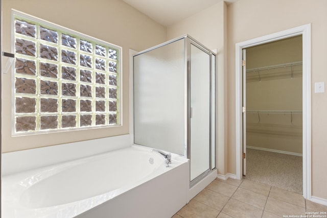 full bathroom featuring tile patterned flooring, a shower stall, a walk in closet, baseboards, and a bath