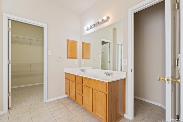 bathroom with tile patterned flooring, a walk in closet, baseboards, double vanity, and a sink