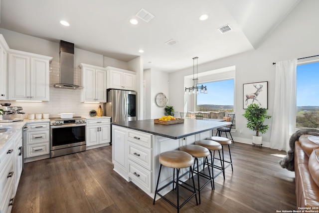 kitchen with visible vents, a breakfast bar, dark wood finished floors, stainless steel appliances, and wall chimney range hood