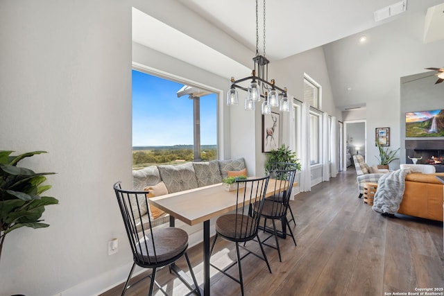 dining space with wood finished floors, baseboards, visible vents, a lit fireplace, and a towering ceiling