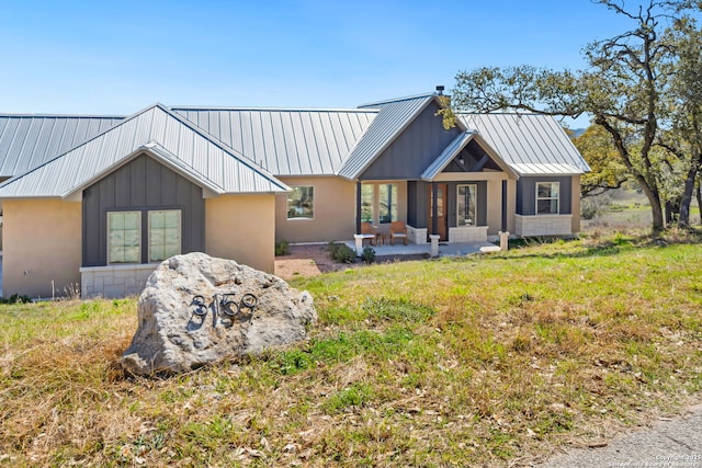 view of front facade with metal roof, a patio, a chimney, and a standing seam roof