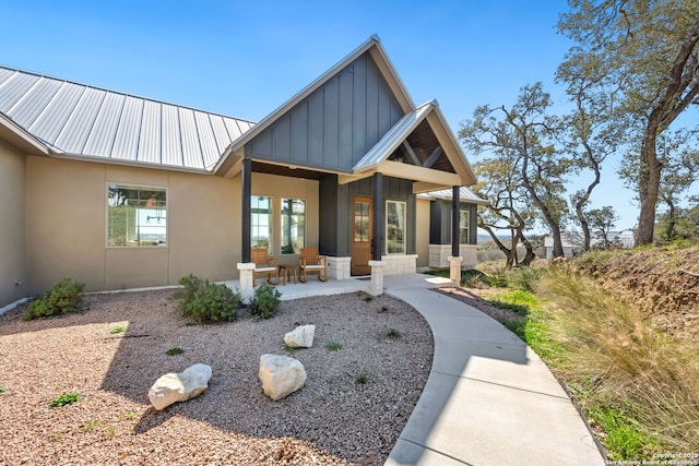 view of front of property with a porch, stucco siding, board and batten siding, and metal roof