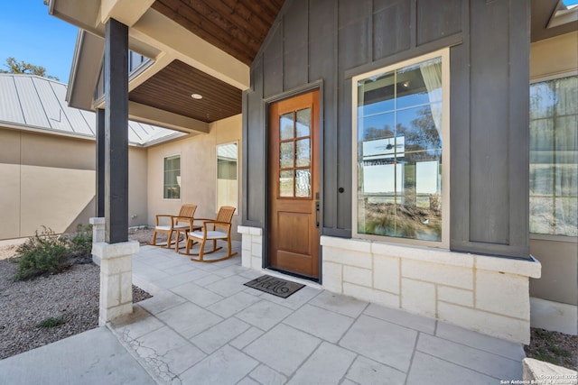 view of exterior entry with a porch, board and batten siding, and metal roof