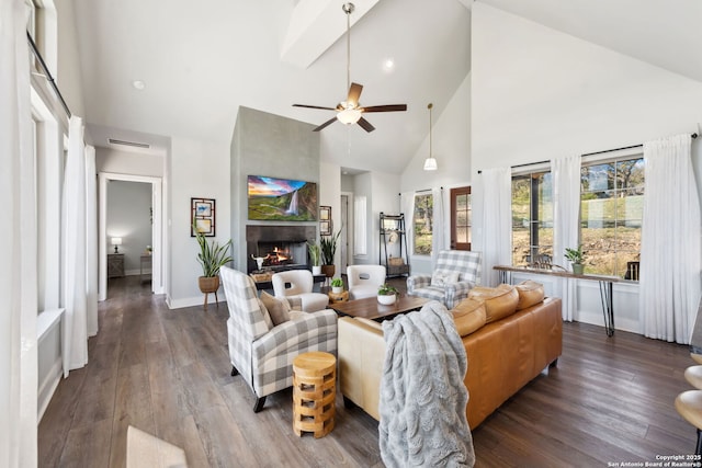 living area with high vaulted ceiling, a ceiling fan, a warm lit fireplace, baseboards, and dark wood-style flooring