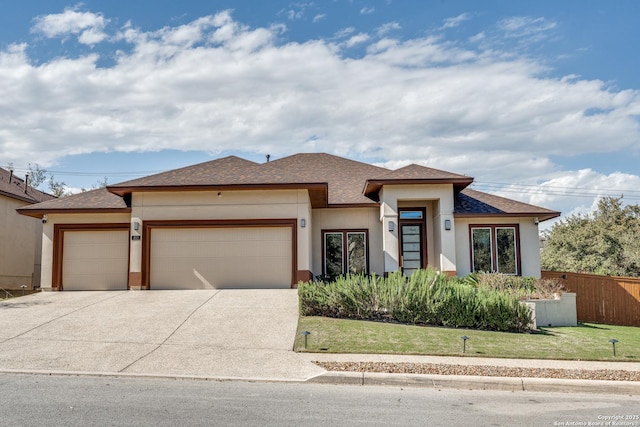 prairie-style house featuring stucco siding, fence, concrete driveway, a front yard, and a garage