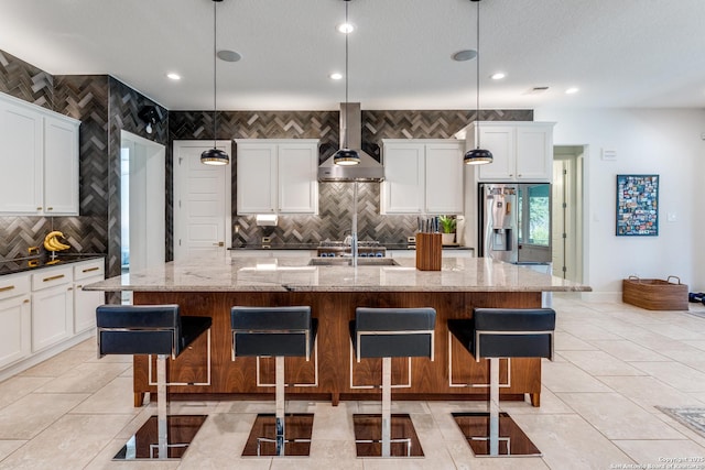 kitchen featuring a breakfast bar area, wall chimney exhaust hood, light tile patterned flooring, and stainless steel refrigerator with ice dispenser