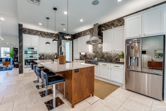 kitchen featuring light stone countertops, visible vents, a sink, appliances with stainless steel finishes, and wall chimney range hood