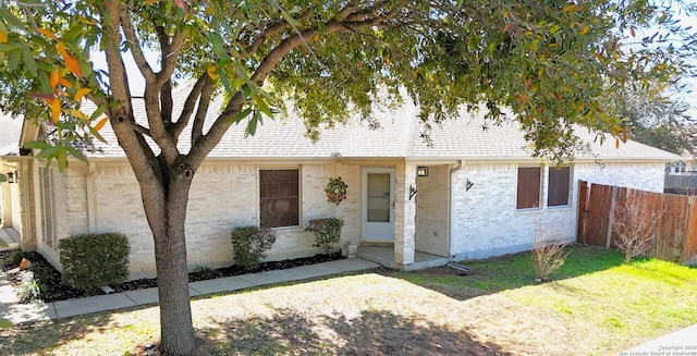 view of front facade with brick siding, roof with shingles, a front yard, and fence