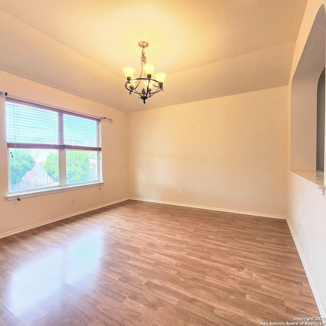 empty room with arched walkways, baseboards, an inviting chandelier, and wood finished floors