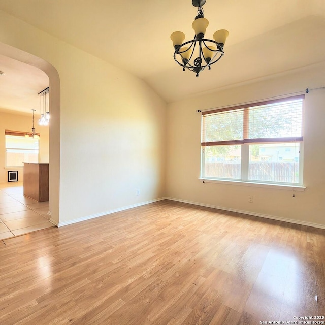 spare room featuring baseboards, an inviting chandelier, arched walkways, vaulted ceiling, and light wood-type flooring