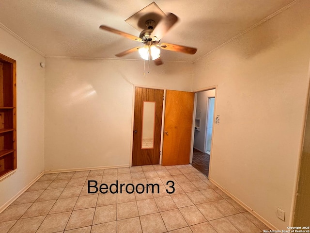 unfurnished room with built in shelves, ceiling fan, ornamental molding, light tile patterned flooring, and a textured ceiling