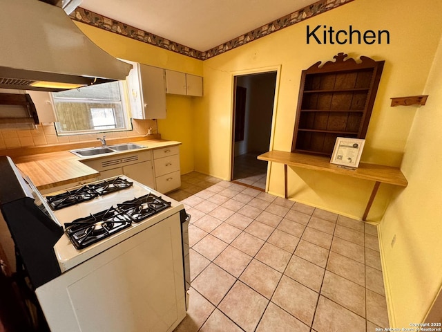 kitchen featuring light countertops, white range with gas cooktop, range hood, light tile patterned flooring, and a sink