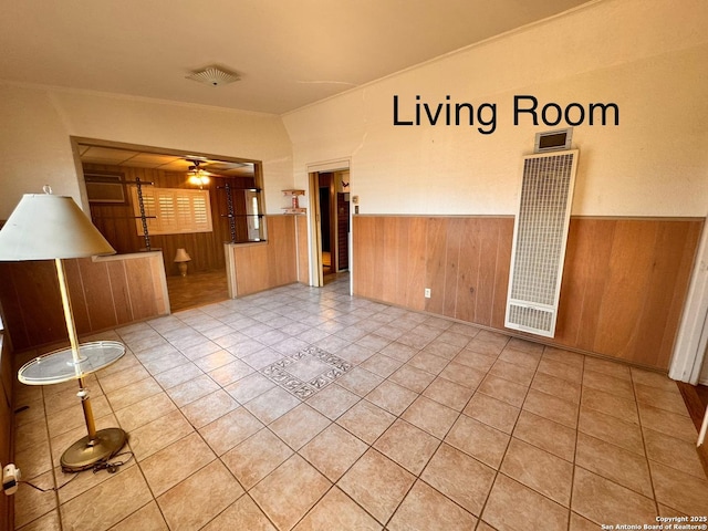 spare room featuring wooden walls, a wainscoted wall, a heating unit, ceiling fan, and tile patterned floors