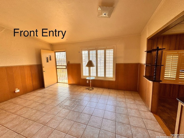 tiled empty room with wooden walls, ornamental molding, and wainscoting