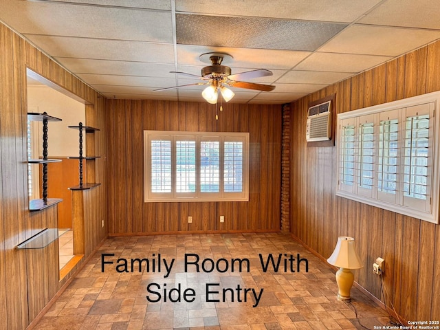 unfurnished room with wooden walls, a ceiling fan, and a drop ceiling