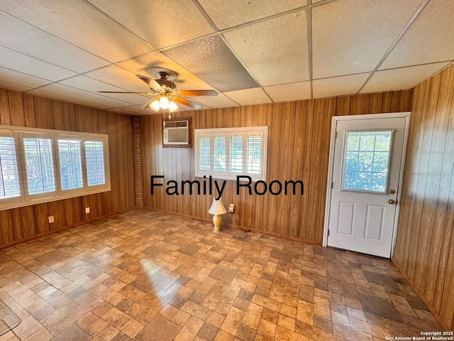 interior space featuring a drop ceiling, wood walls, an AC wall unit, and a ceiling fan