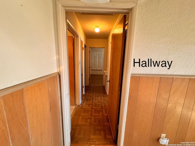 corridor with wooden walls, a textured wall, and wainscoting