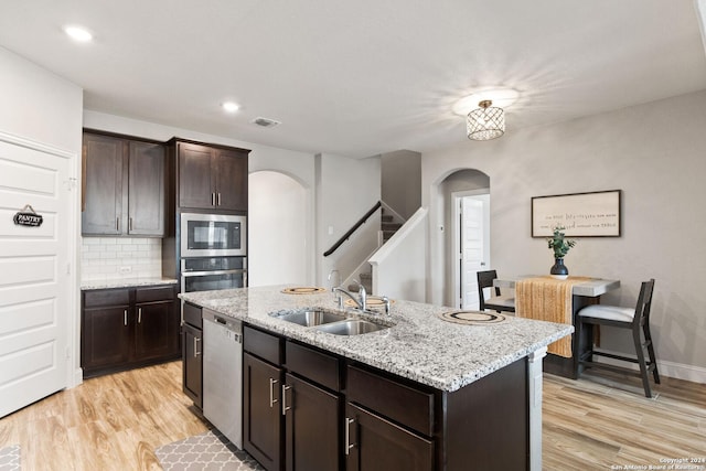 kitchen featuring a sink, light wood-type flooring, arched walkways, and appliances with stainless steel finishes