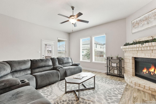 living area featuring ceiling fan, baseboards, a stone fireplace, and wood finished floors