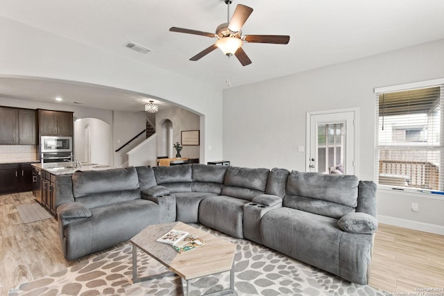 living room featuring ceiling fan, visible vents, arched walkways, and light wood-style flooring