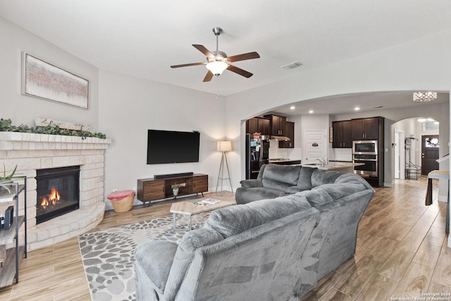 living room featuring light wood-type flooring, visible vents, arched walkways, and a glass covered fireplace