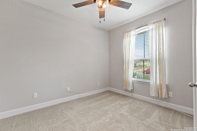 spare room featuring light colored carpet, a ceiling fan, and baseboards