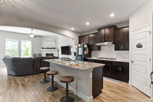 kitchen with light wood-type flooring, stainless steel gas stovetop, black fridge with ice dispenser, under cabinet range hood, and open floor plan