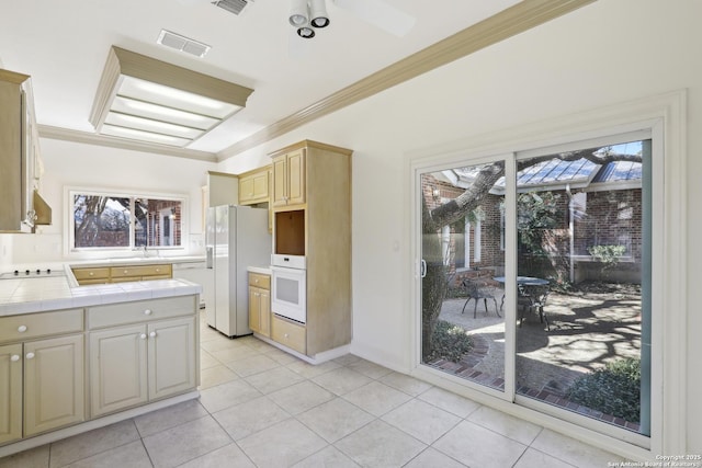 kitchen featuring visible vents, crown molding, tile counters, white appliances, and a sink