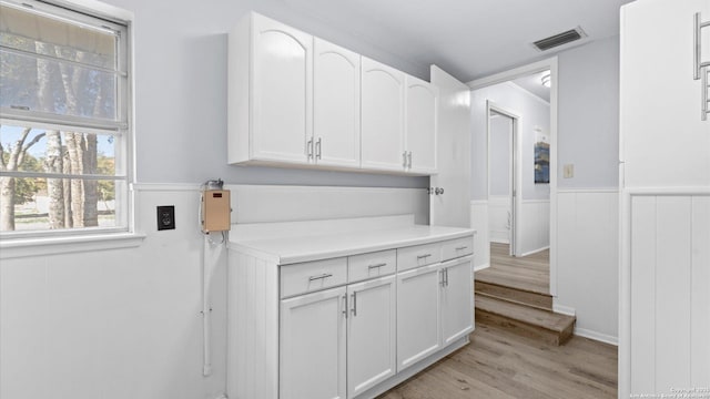 interior space with light wood-type flooring, visible vents, a wainscoted wall, white cabinets, and light countertops