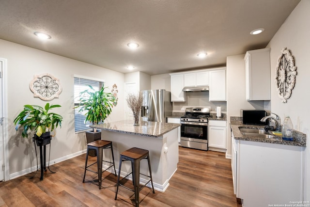 kitchen with a breakfast bar area, wood finished floors, under cabinet range hood, appliances with stainless steel finishes, and a center island