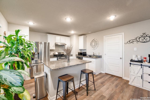 kitchen featuring a sink, white cabinets, under cabinet range hood, appliances with stainless steel finishes, and a kitchen breakfast bar