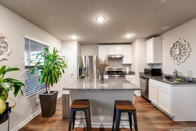 kitchen featuring under cabinet range hood, appliances with stainless steel finishes, a kitchen breakfast bar, dark wood-style floors, and a sink