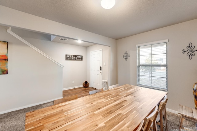 dining space featuring wood finished floors, baseboards, visible vents, and a textured ceiling