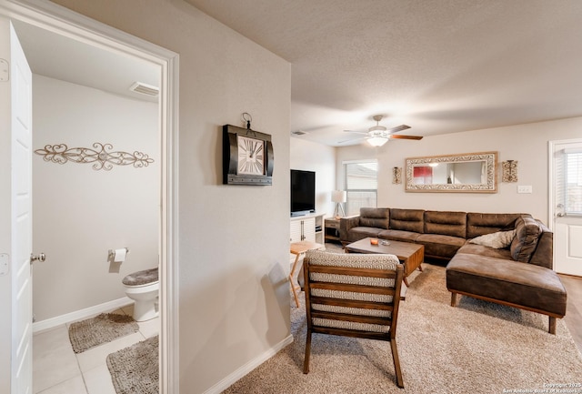 living area featuring light tile patterned floors, a ceiling fan, baseboards, visible vents, and a textured ceiling