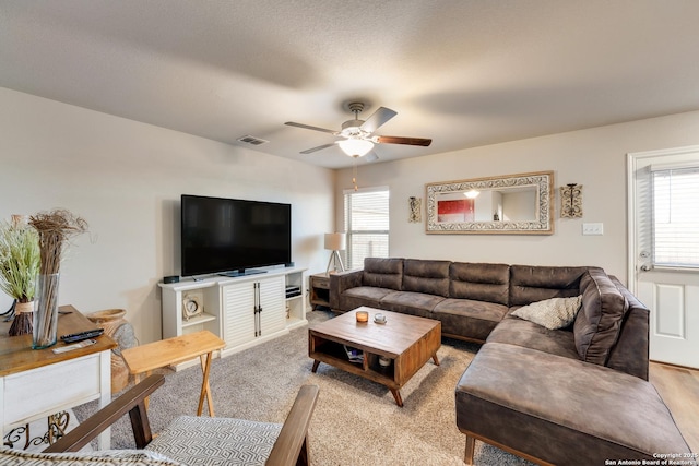 living room with a wealth of natural light, visible vents, light colored carpet, and a ceiling fan