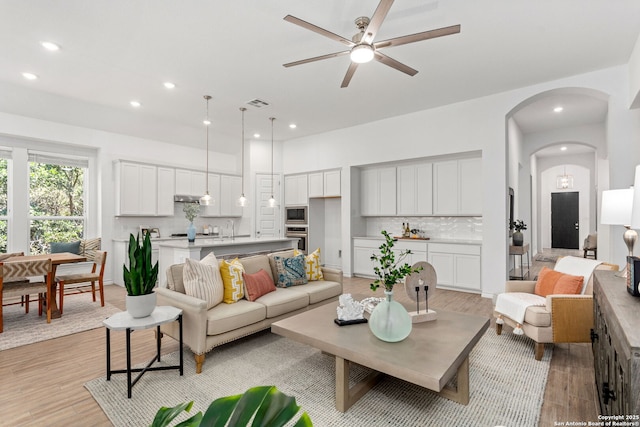 living area featuring light wood-style floors, recessed lighting, visible vents, and arched walkways