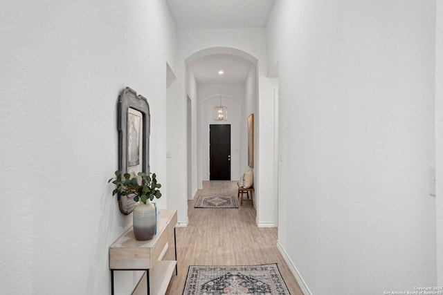 hallway featuring light wood-type flooring, arched walkways, and baseboards