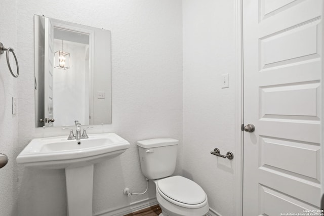 bathroom with toilet, a textured wall, baseboards, and a sink