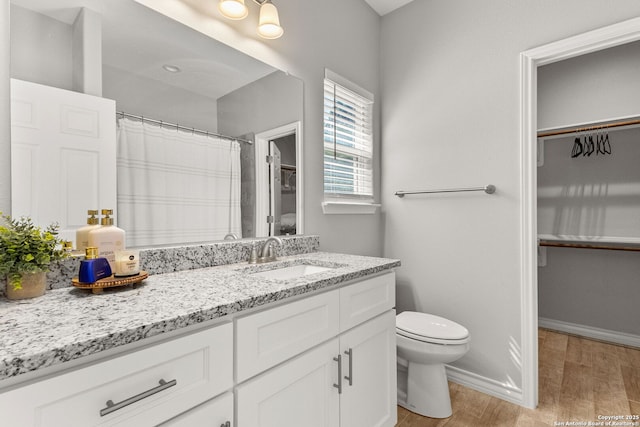 full bath featuring a walk in closet, baseboards, toilet, wood finished floors, and vanity