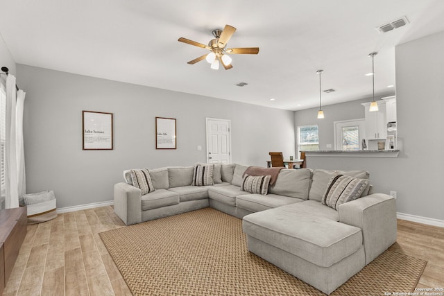 living area featuring visible vents, baseboards, light wood-style floors, and a ceiling fan