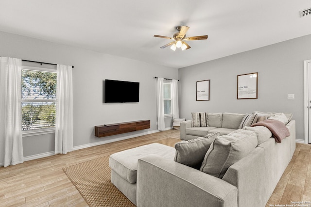 living room featuring ceiling fan, visible vents, baseboards, and light wood-style flooring