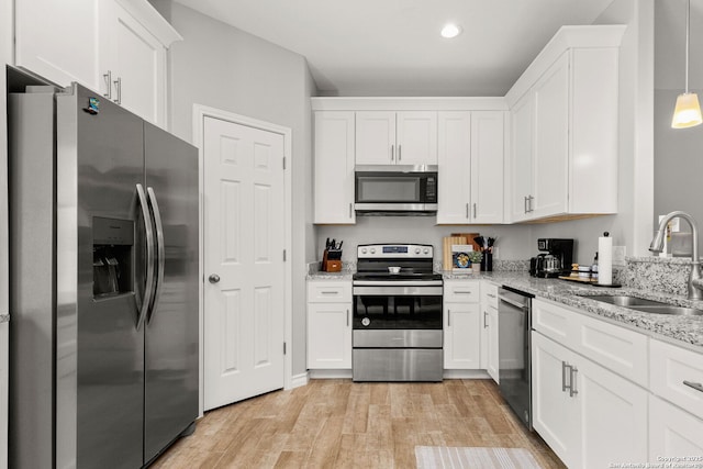 kitchen with a sink, white cabinetry, stainless steel appliances, light wood finished floors, and light stone countertops