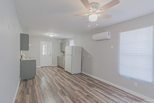 kitchen with wood finished floors, baseboards, a wall mounted AC, freestanding refrigerator, and gray cabinetry